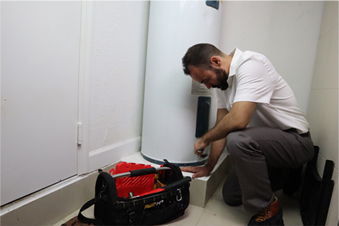 Professional technician performing water damage restoration by inspecting a water heater, with tools and equipment nearby.