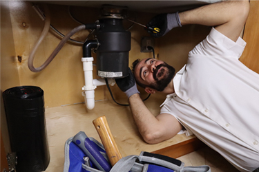 Plumber repairing a water pipe under a sink, demonstrating professional sewage cleanup and water restoration services.